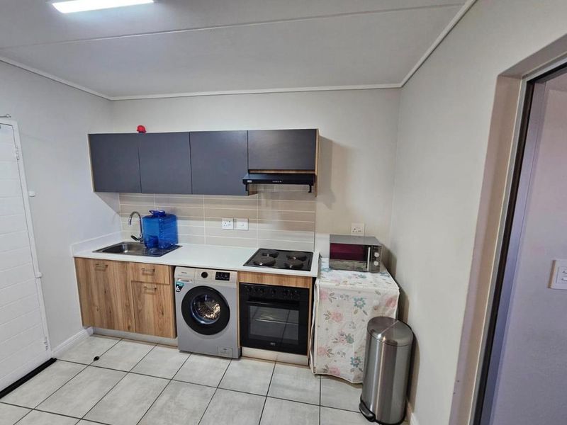Compact kitchen featuring modern wood-grain and dark grey cabinetry, integrated oven and hob, tiled backsplash, and tiled flooring.