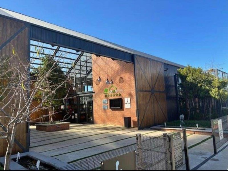 Modern industrial-style building exterior featuring exposed brickwork, large glass panels, steel framing, and a landscaped courtyard with a water feature.