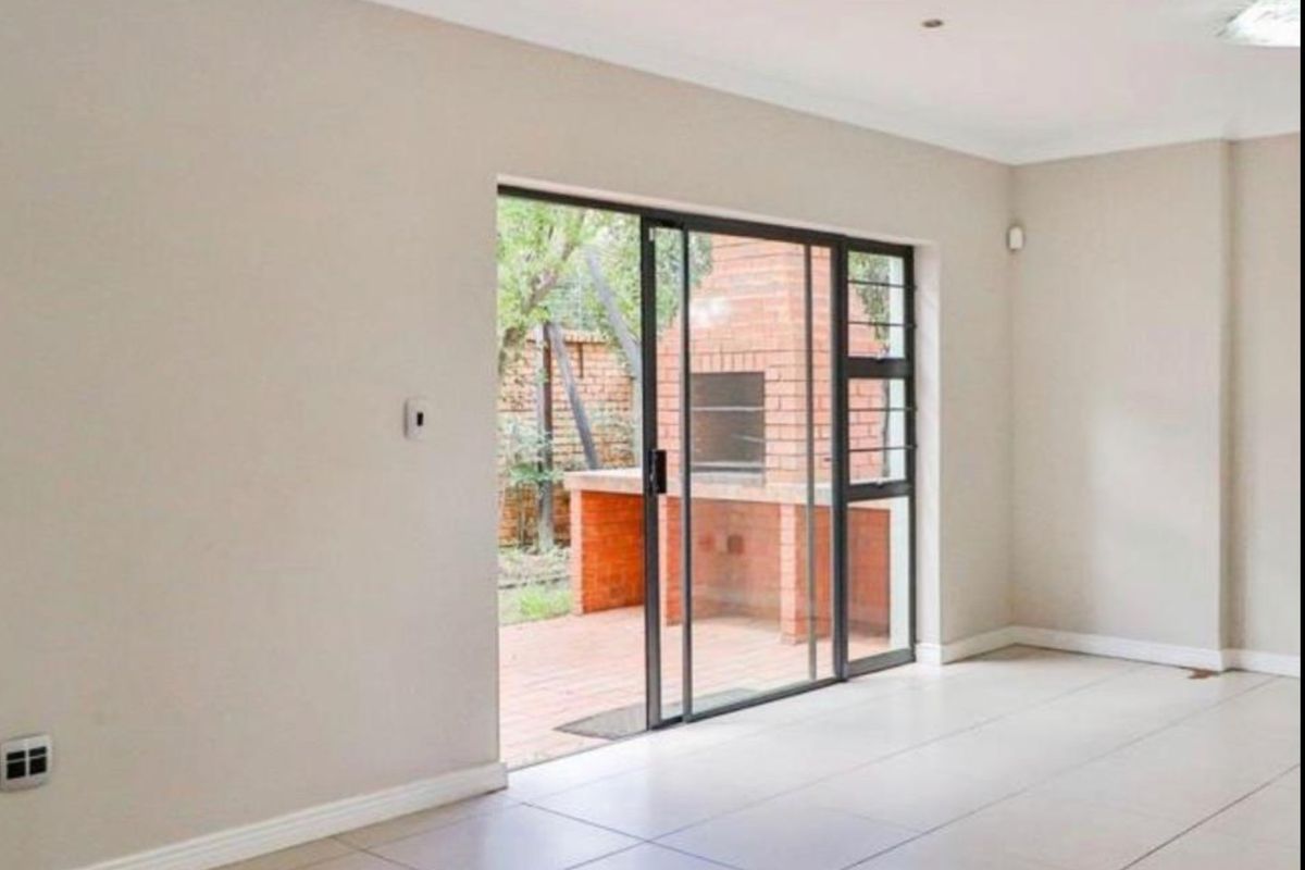 Spacious, light-filled living area featuring neutral tiled flooring and a sliding glass door providing direct access to a private patio with a built-in braai.