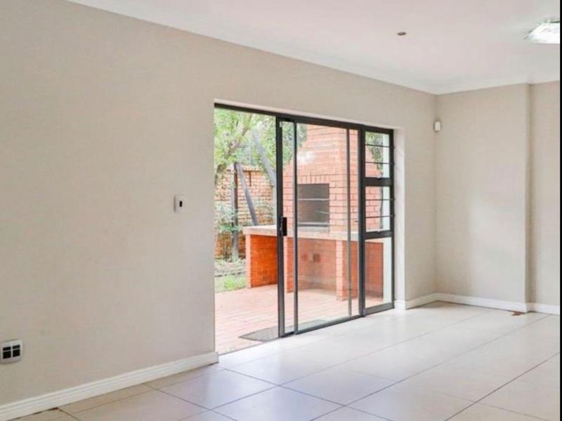 Spacious, light-filled living area featuring neutral tiled flooring and a sliding glass door providing direct access to a private patio with a built-in braai.