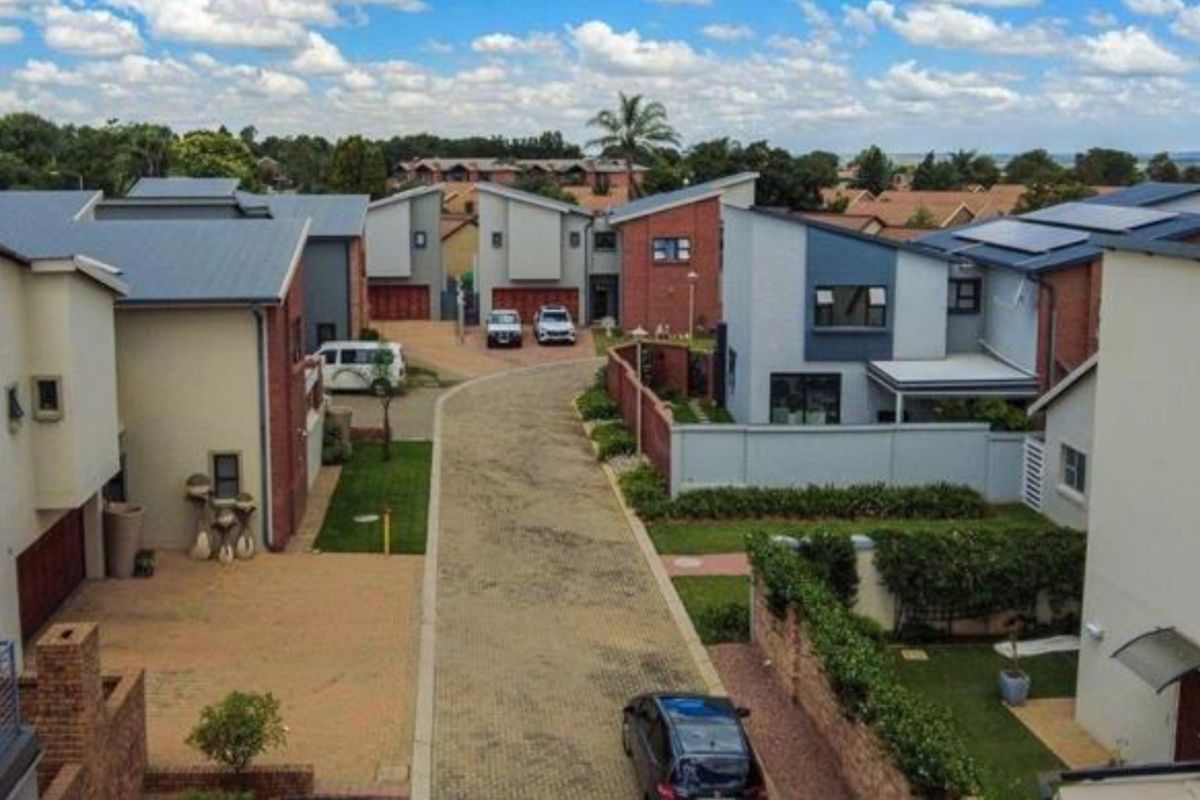 An aerial view of a modern townhouse complex featuring paved driveways, brick and rendered facades, and pitched metal roofing within a residential estate.