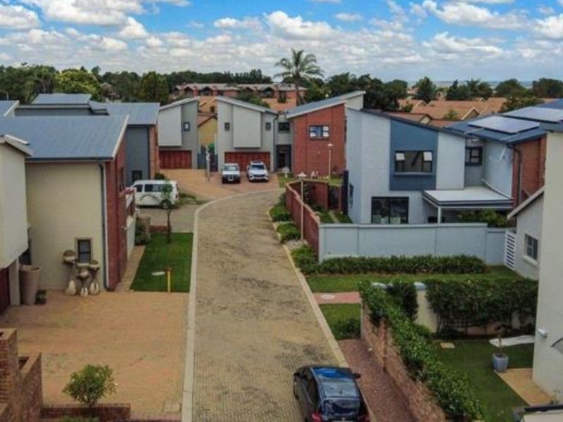 An aerial view of a modern townhouse complex featuring paved driveways, brick and rendered facades, and pitched metal roofing within a residential estate.