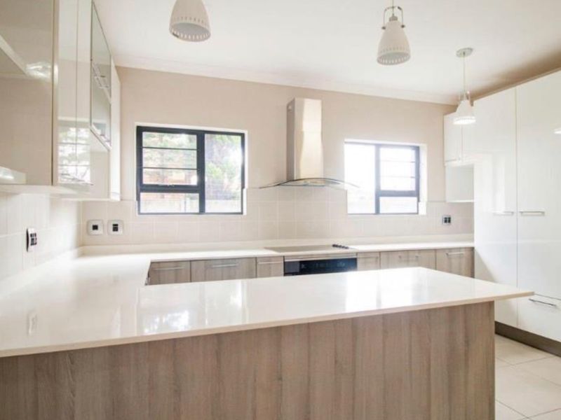 Modern kitchen featuring sleek white and wood-tone cabinetry, stone countertops, integrated hob with extractor fan, and tiled flooring in a bright, open layout.