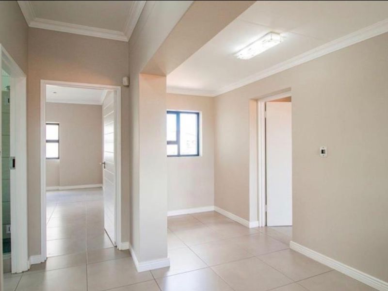 A clean, neutral-toned hallway featuring tiled flooring, crisp cornicing, and multiple doorways leading to adjacent rooms.
