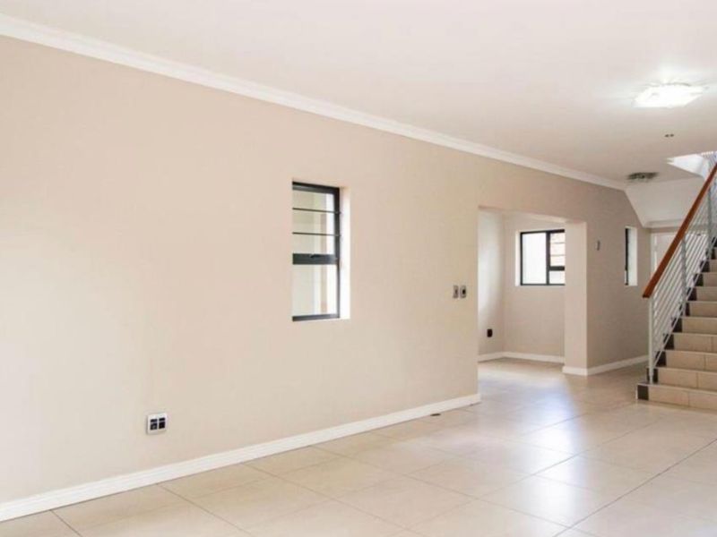 Spacious open-plan living area featuring neutral tiled flooring, a modern staircase with metal balustrades, and clean finishes throughout.