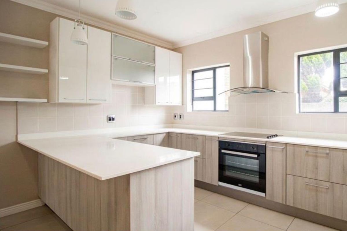 Modern kitchen featuring light wood-grain cabinetry, white stone countertops, built-in oven and hob, stainless steel extractor fan, and neutral tiled finishes.
