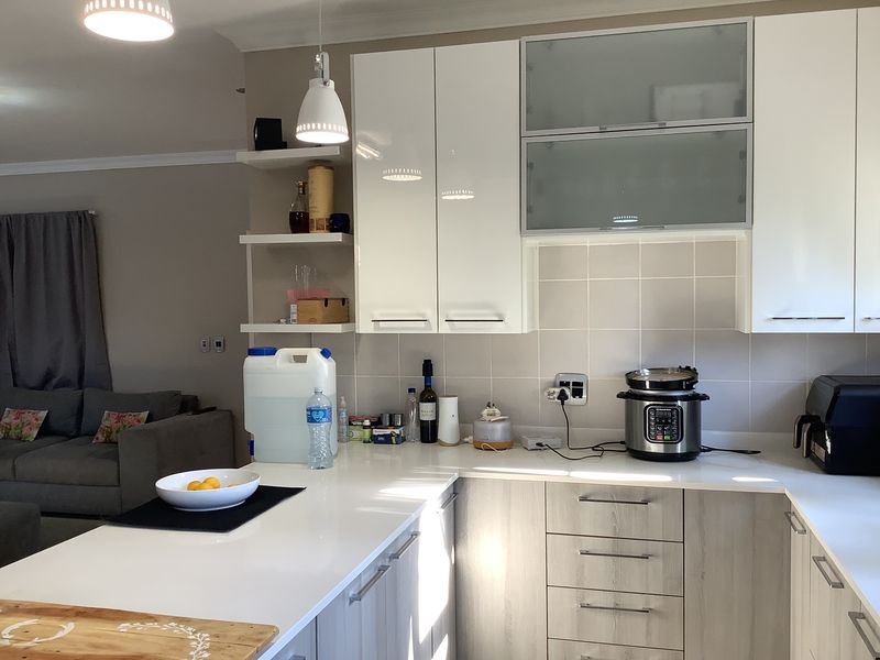 Modern open-plan kitchen featuring high-gloss white upper cabinets, wood-grain lower cabinetry, quartz countertops, and a tiled backsplash, seamlessly integrated with the living area.