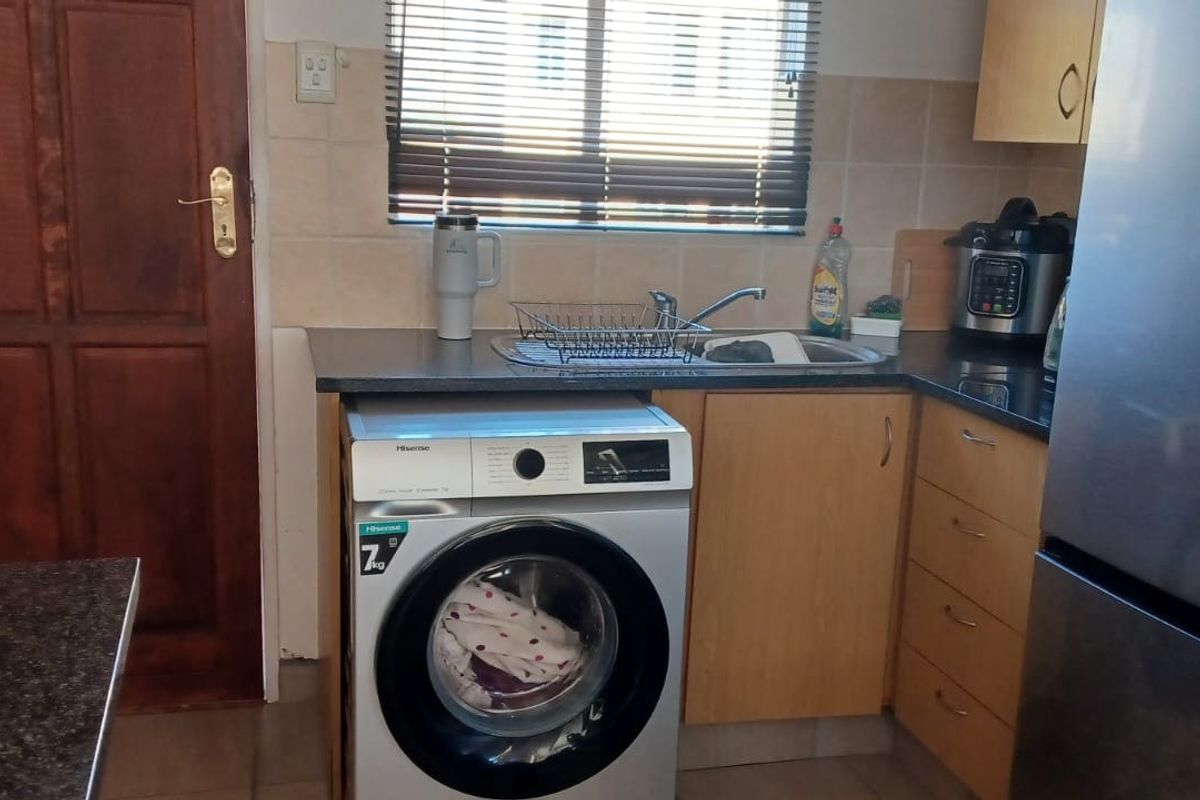 Compact kitchen featuring granite countertops, laminate cabinetry, and a tiled backsplash, providing a functional workspace with integrated plumbing for laundry appliances.