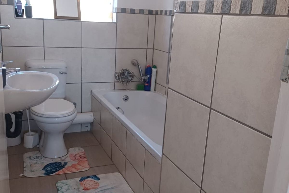 A functional bathroom featuring a bathtub, pedestal basin, and toilet with neutral wall and floor tiling.