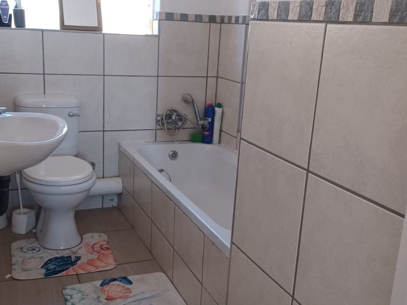 A functional bathroom featuring a bathtub, pedestal basin, and toilet with neutral wall and floor tiling.