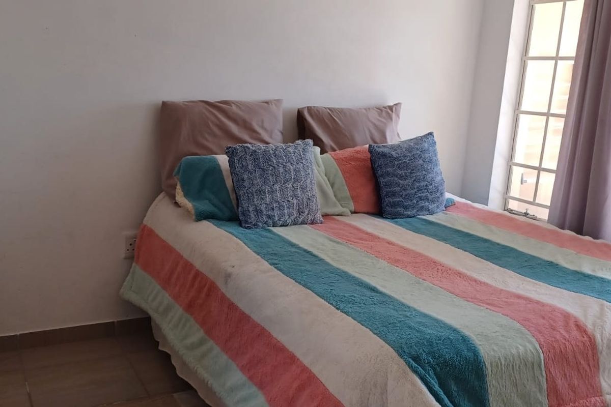A standard bedroom featuring tiled flooring and a window fitted with security bars, providing natural light.