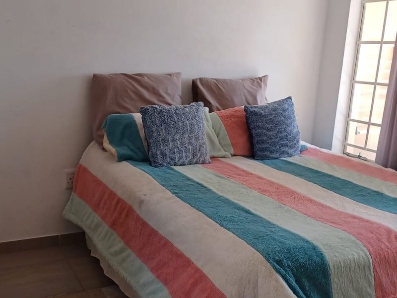 A standard bedroom featuring tiled flooring and a window fitted with security bars, providing natural light.