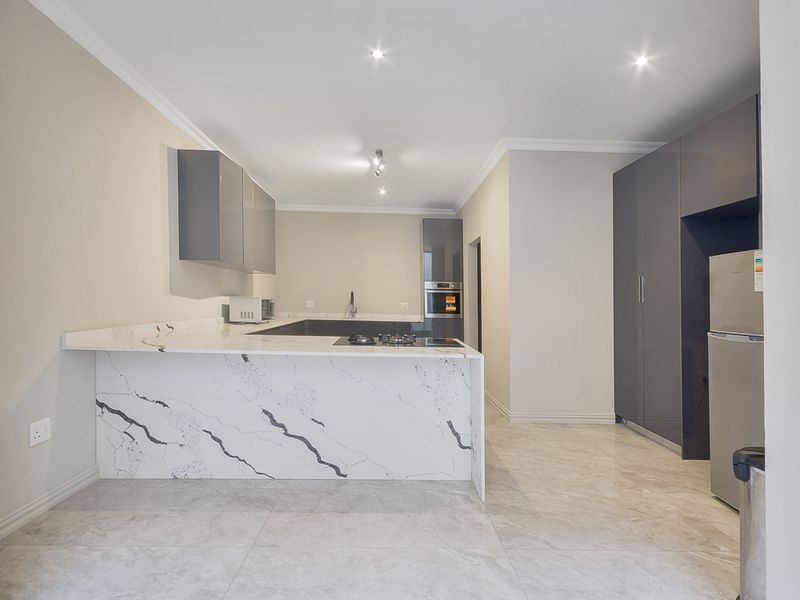 Modern kitchen featuring high-gloss cabinetry, marble-look stone countertops, a built-in oven, and a gas hob, finished with sleek tiled flooring.