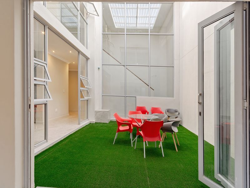 A bright, modern enclosed courtyard featuring artificial turf, high double-volume glass walls, and a large skylight, providing a seamless indoor-outdoor transition.