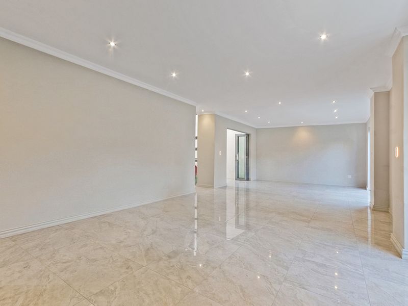 A spacious, empty open-plan living area featuring polished porcelain tile flooring, recessed downlighting, and neutral wall finishes.