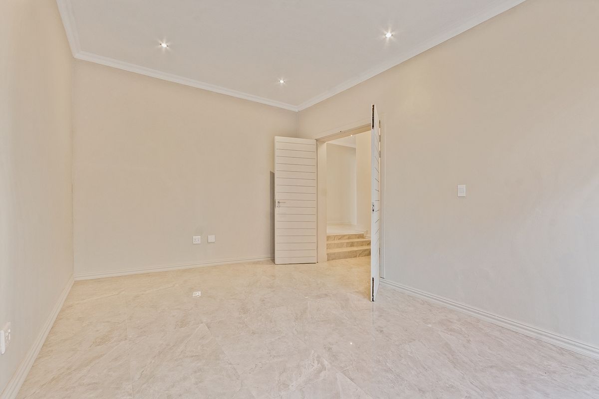 A bright, vacant bedroom featuring neutral walls, polished marble-look floor tiles, recessed downlights, and clean architectural finishes.