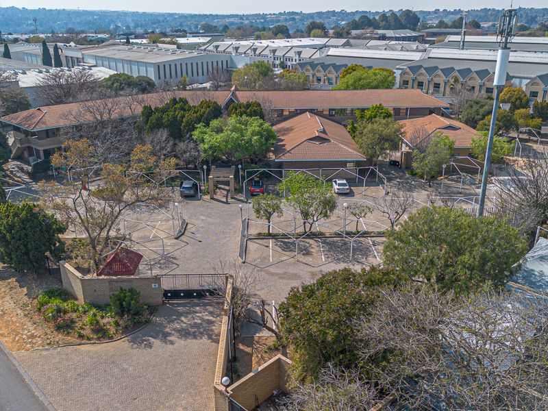 Aerial view of a commercial property complex featuring a paved parking area, secure gated entrance, and multiple buildings with tiled roofing.