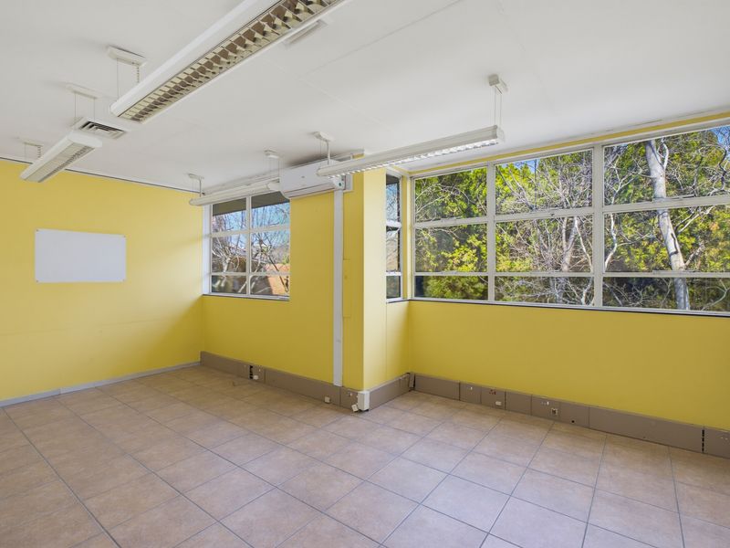 A bright, empty office space featuring tiled flooring, large windows with natural light, and integrated ceiling lighting.