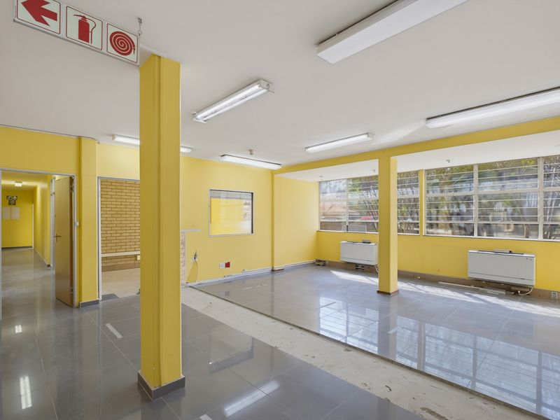 Open-plan commercial office space featuring tiled flooring, structural columns, large windows, and integrated air conditioning units, ready for professional fit-out.