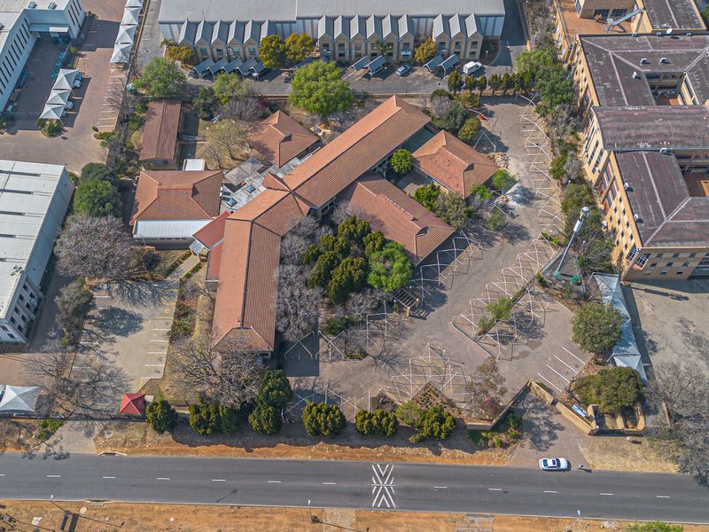 Aerial view of a commercial property complex featuring multiple buildings with tiled roofs, extensive paved parking areas, and established landscaping.
