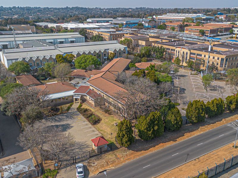 Aerial view of a commercial property complex featuring multiple buildings, tiled roofing, paved parking areas, and established landscaping within a secure perimeter.