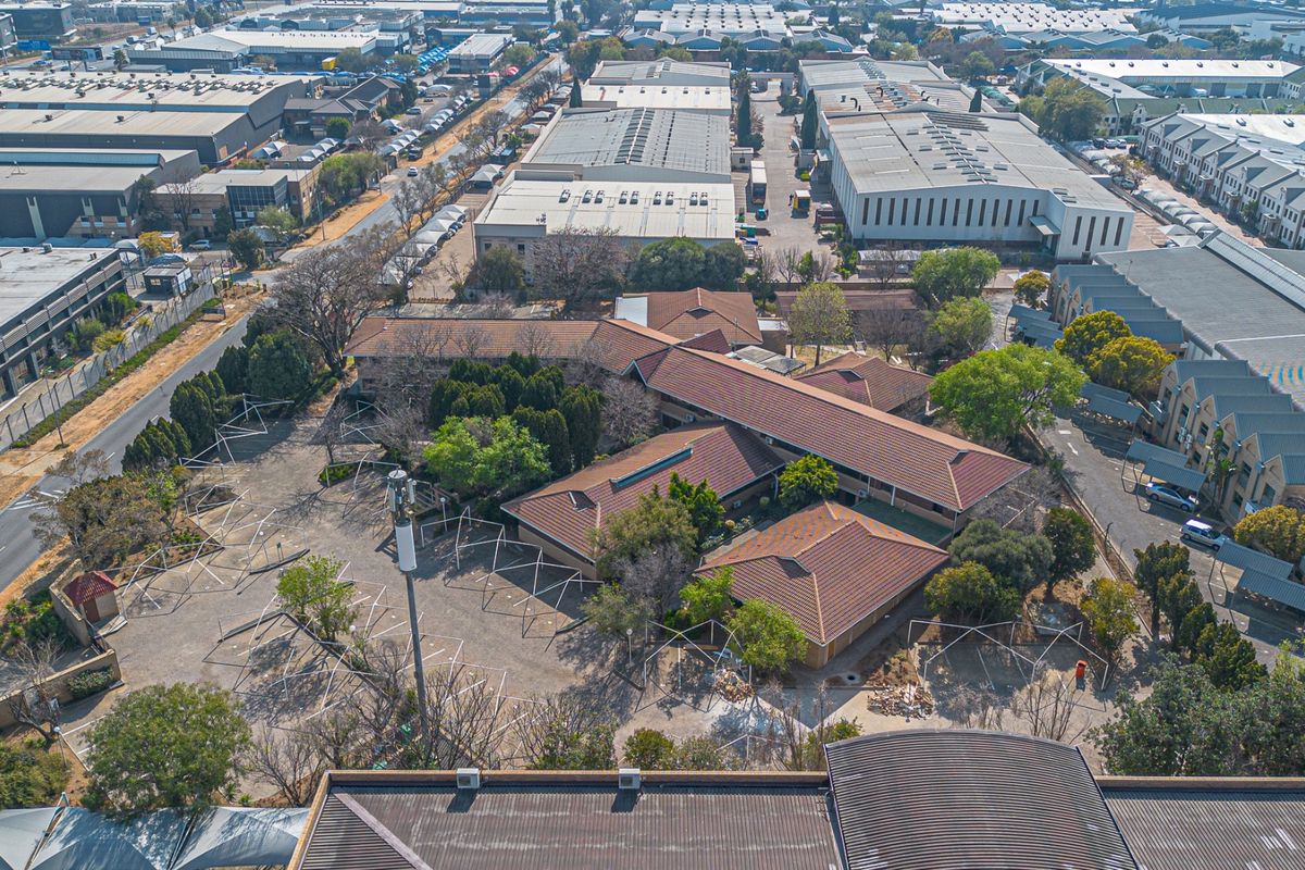 Aerial view of a commercial property complex featuring multiple buildings with tiled roofs, extensive paved parking areas, and established landscaping within an industrial park setting.