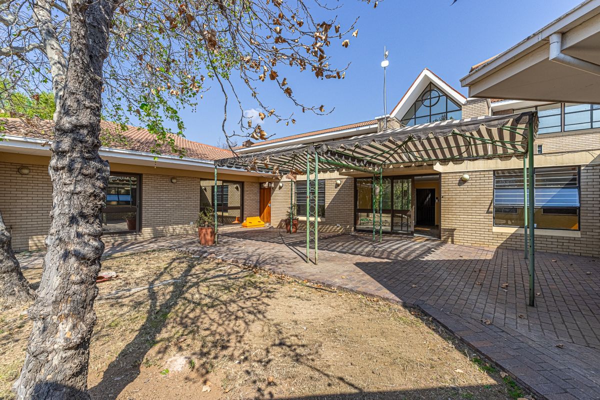 Rear view of the commercial property featuring a paved patio area, metal pergola structure, and brick facade with multiple access points.