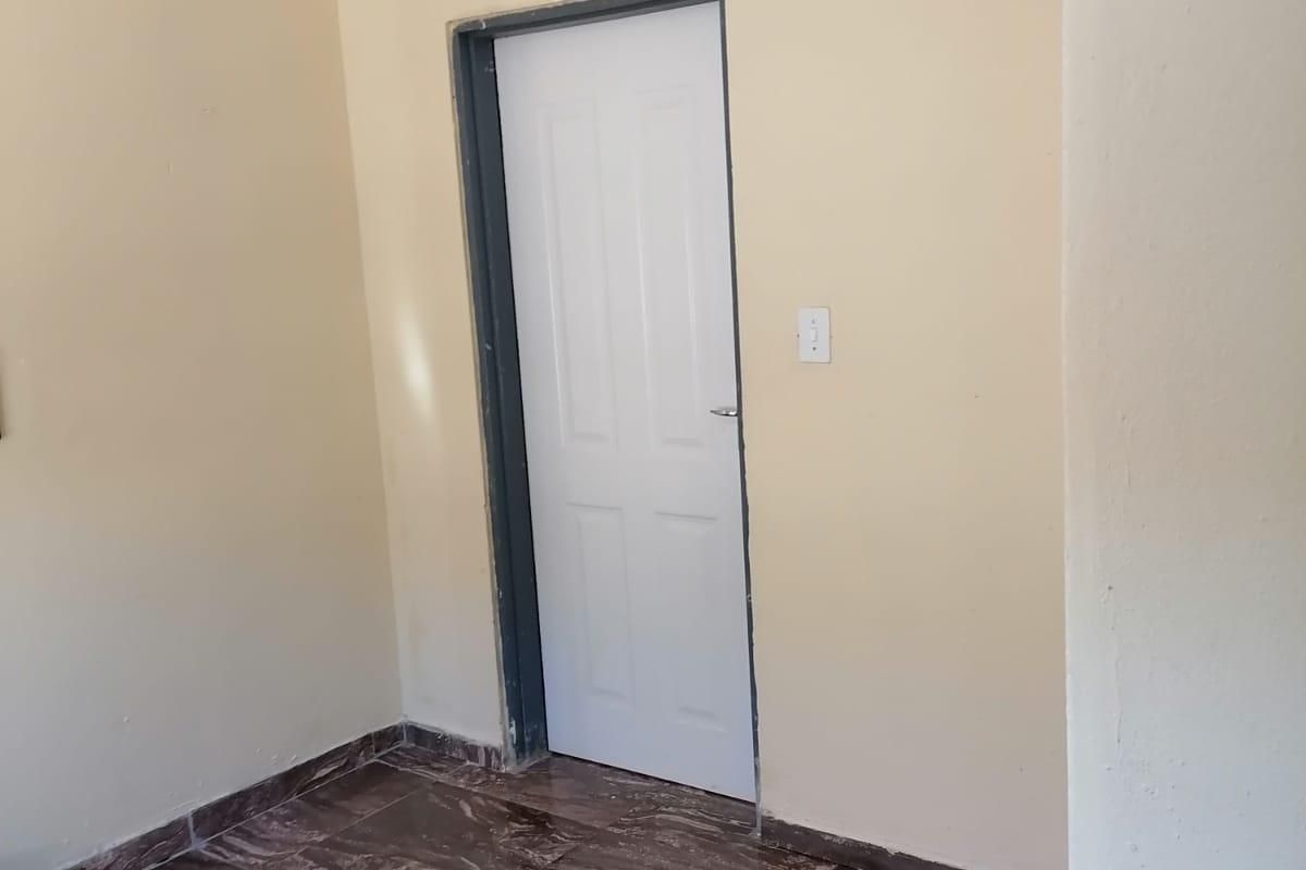 An empty bedroom featuring tiled flooring, cove cornicing, and an unfinished door frame, offering a blank canvas for renovation.
