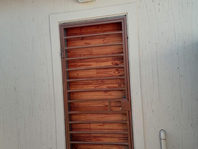 Exterior view of a rear entrance featuring a wooden door with a metal security gate and external wall lighting.