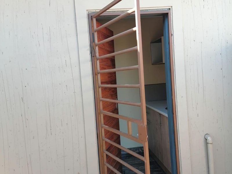 Exterior view of a rear entrance featuring a metal security gate, textured wall finish, and exposed roof rafters.