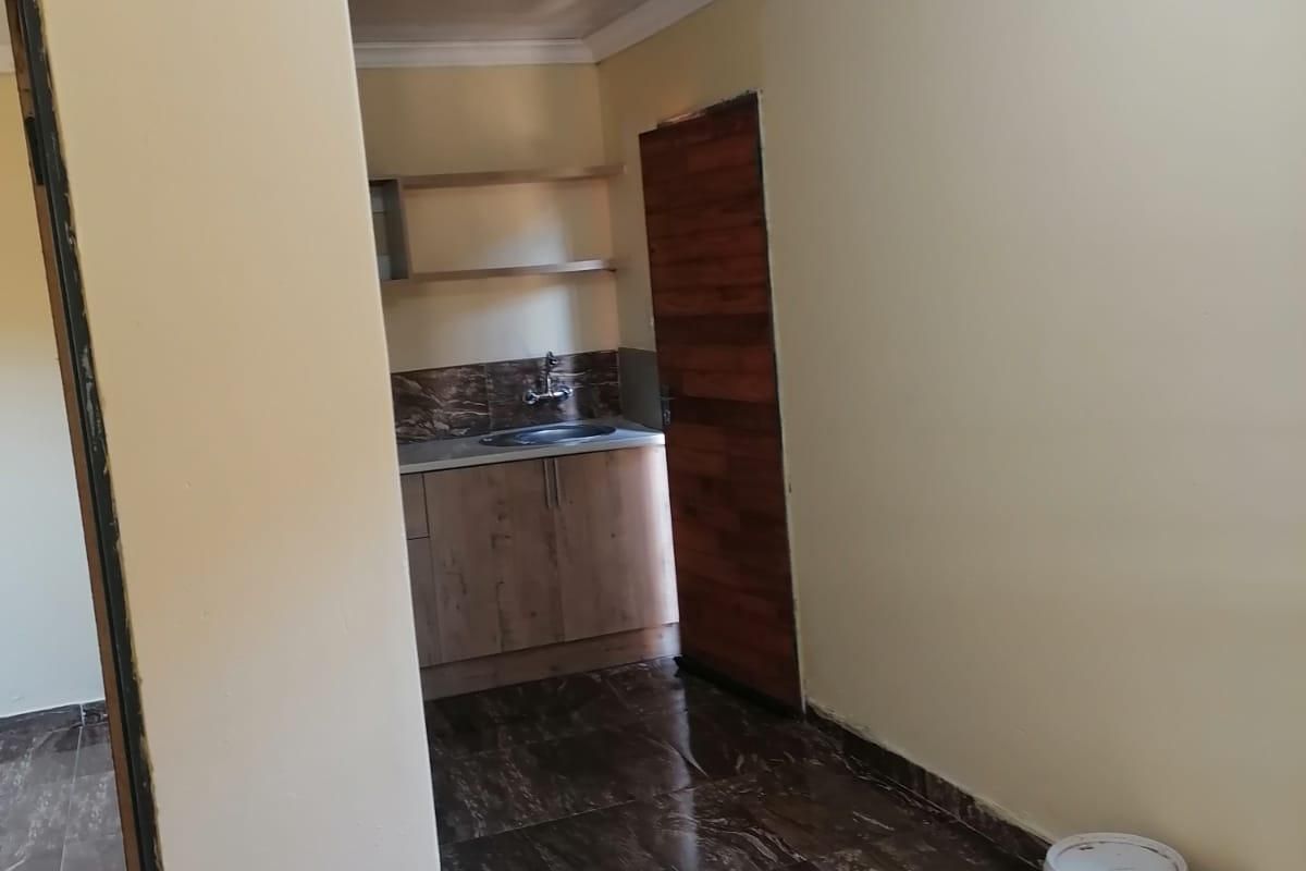 A compact kitchen area featuring dark marble-effect floor tiles, wooden cabinetry, and a sink, presented in a clean, vacant state.