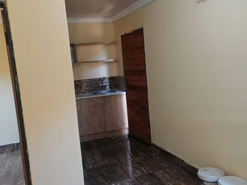 A compact kitchen area featuring dark marble-effect floor tiles, wooden cabinetry, and a sink, presented in a clean, vacant state.