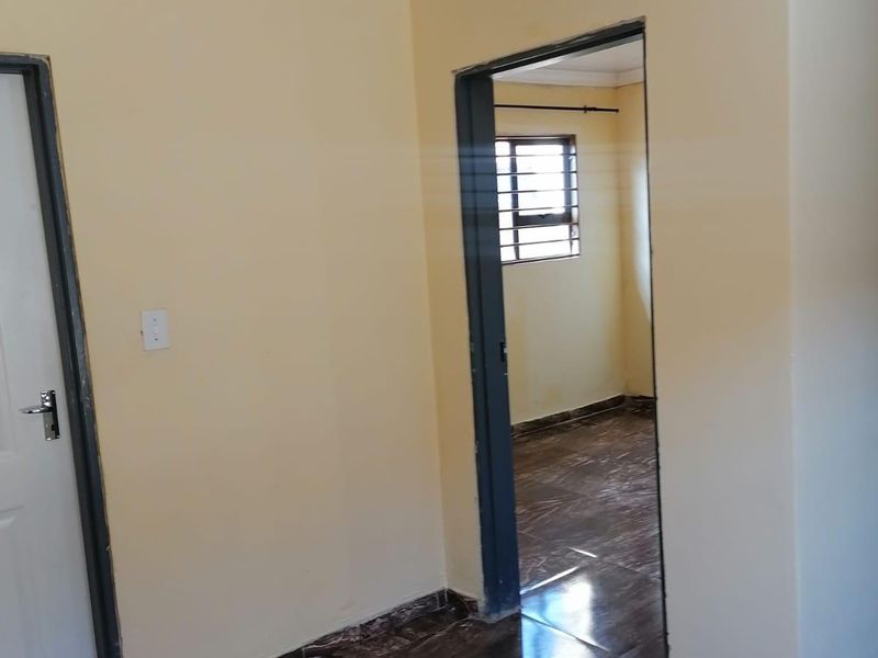 A vacant hallway area featuring dark marble-effect floor tiles, neutral wall paint, and white ceiling cornicing, leading into an adjacent bedroom.