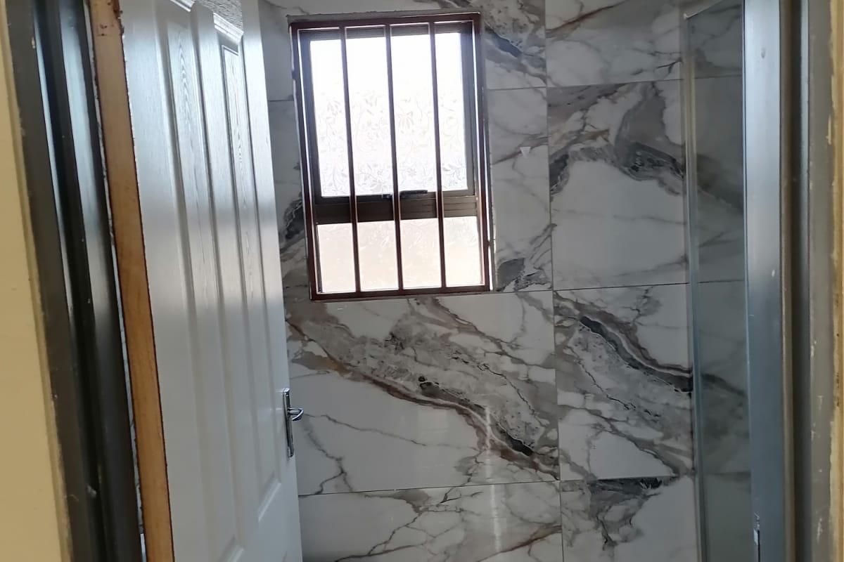 A compact bathroom featuring marble-effect wall tiling, a shower enclosure, and a toilet, viewed through an open doorway.