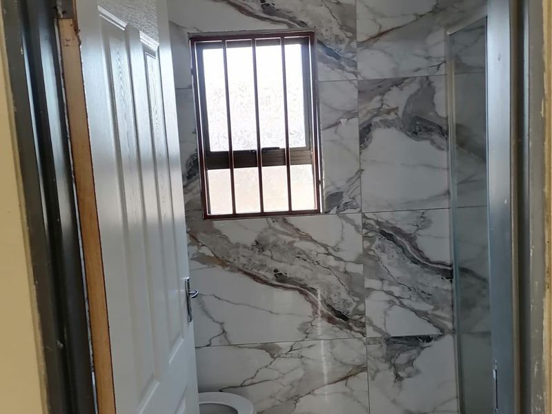 A compact bathroom featuring marble-effect wall tiling, a shower enclosure, and a toilet, viewed through an open doorway.