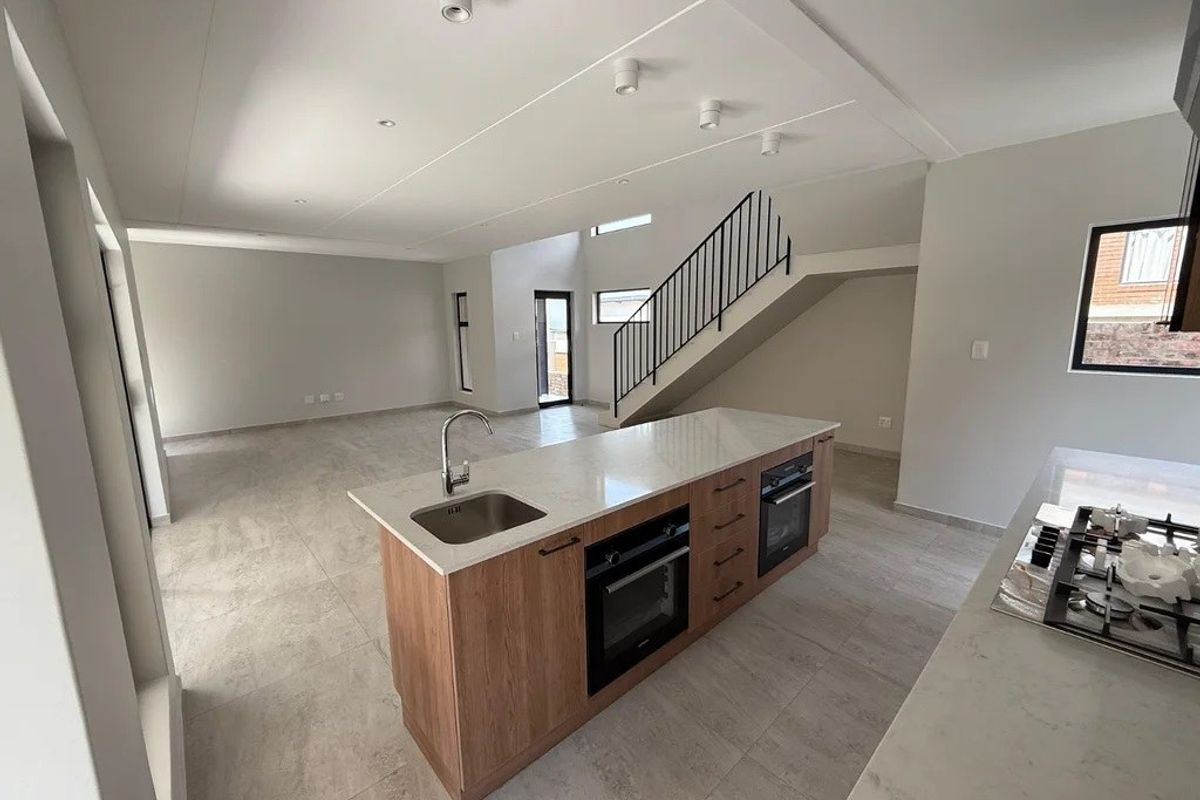 Spacious open-plan living area featuring a modern kitchen with a central island, built-in appliances, stone countertops, and a staircase leading to the upper level.