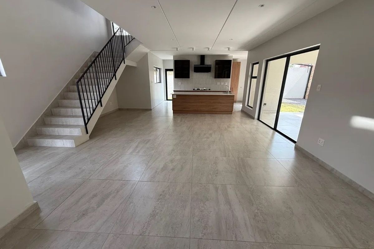 Spacious open-plan living area featuring a modern kitchen with island, sleek tiled flooring, and a staircase, leading out to a private patio area.