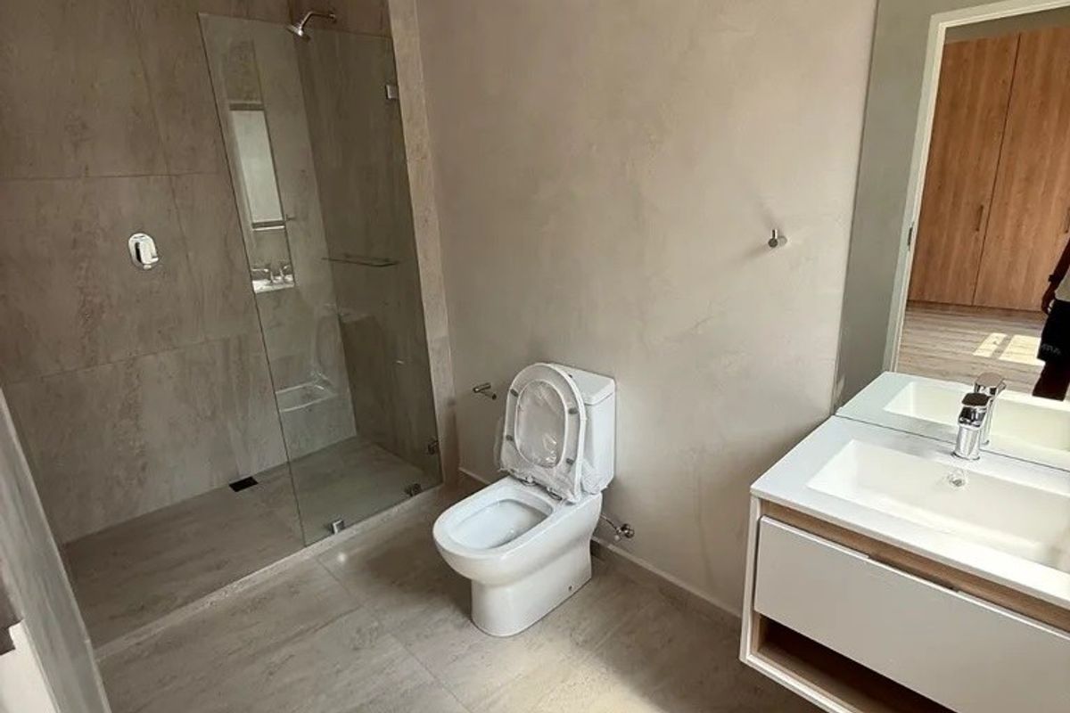 Modern, minimalist bathroom featuring a spacious walk-in shower with glass enclosure, wall-mounted toilet, and a sleek vanity with basin and large mirror.