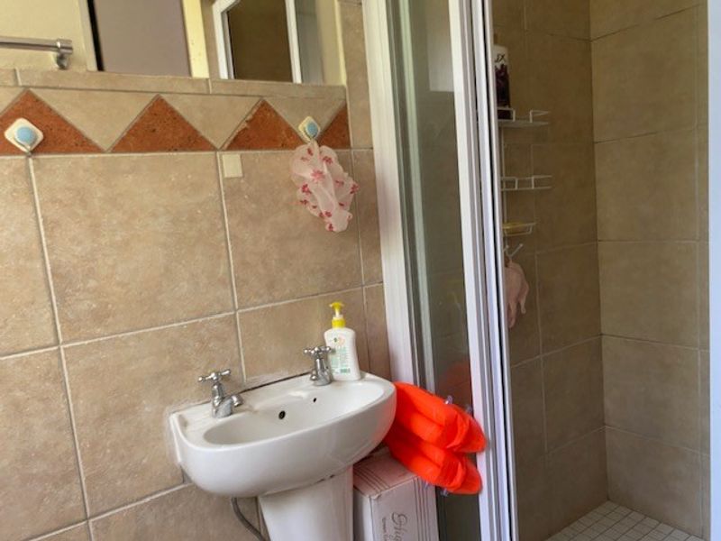 A functional bathroom featuring a pedestal washbasin, shower enclosure, and neutral ceramic wall tiling with decorative accents.