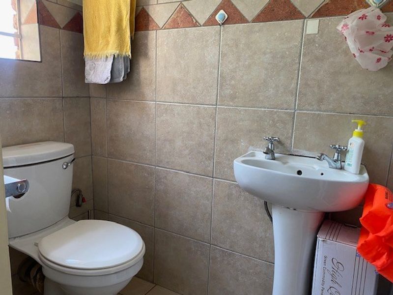 A compact bathroom featuring a pedestal basin and a standard toilet with full-height ceramic wall tiling.