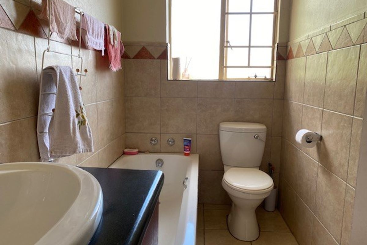 A functional bathroom featuring a bathtub, toilet, and vanity basin with neutral wall and floor tiling.