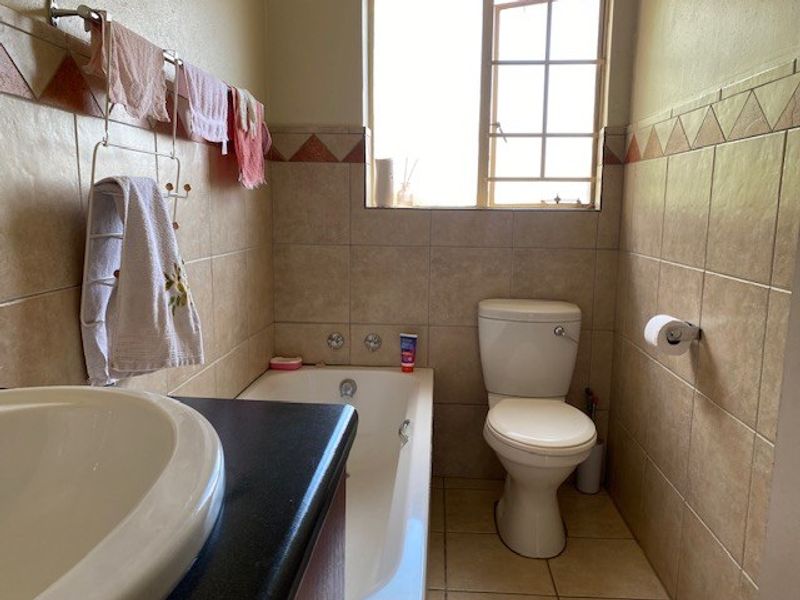 A functional bathroom featuring a bathtub, toilet, and vanity basin with neutral wall and floor tiling.