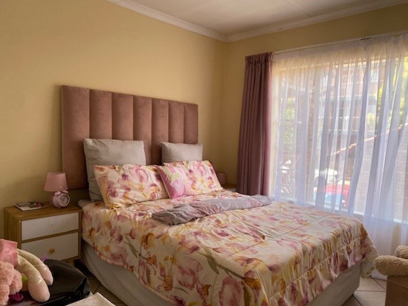 A bedroom featuring tiled flooring and large windows with curtain rails, providing natural light and a view of the exterior.