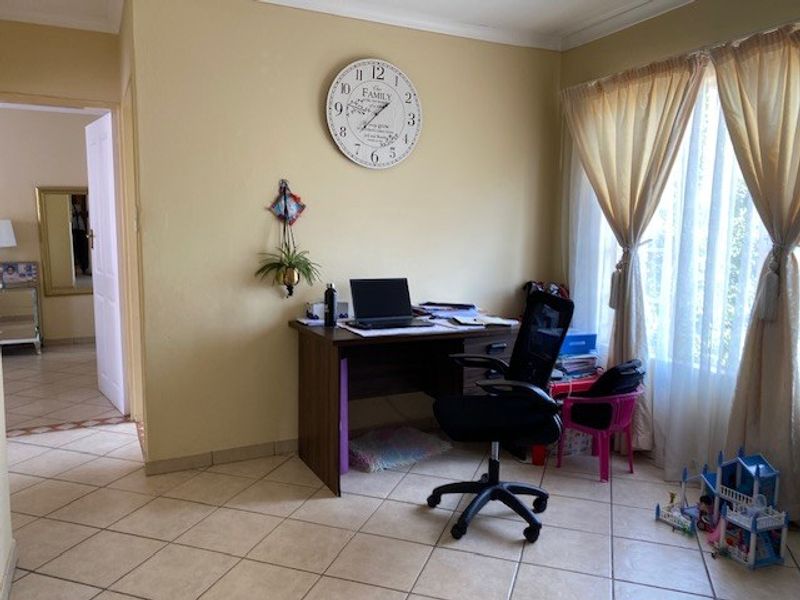 A living area featuring neutral wall paint, tiled flooring, and coved ceiling cornices, currently utilized as a home office space.