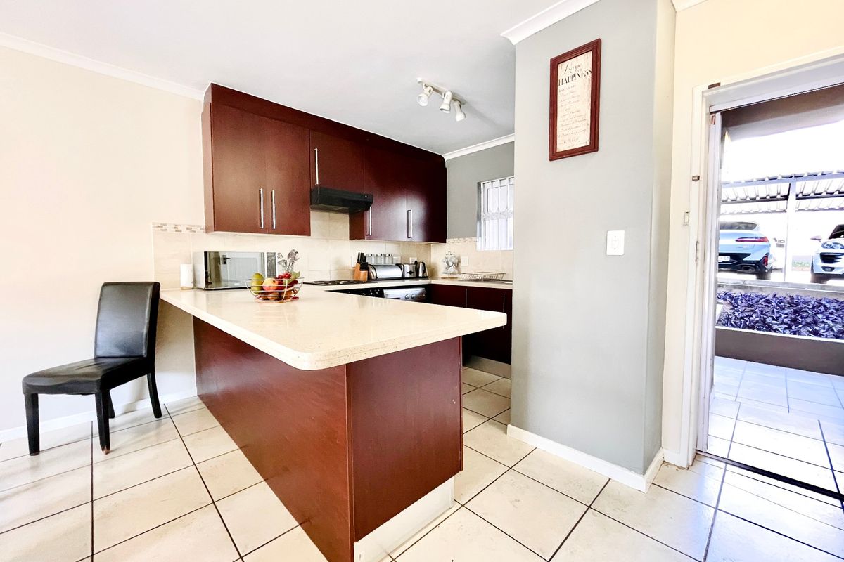 A functional kitchen featuring dark wood cabinetry, stone countertops, a breakfast bar, and ceramic floor tiles, with direct access to the exterior.