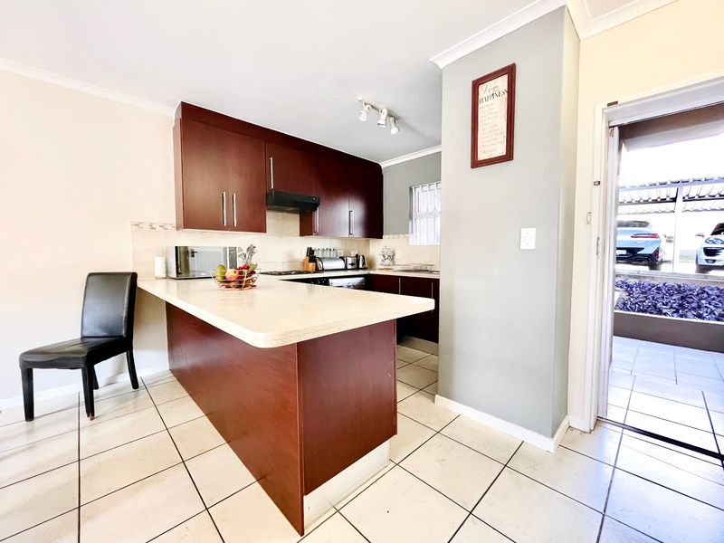 A functional kitchen featuring dark wood cabinetry, stone countertops, a breakfast bar, and ceramic floor tiles, with direct access to the exterior.