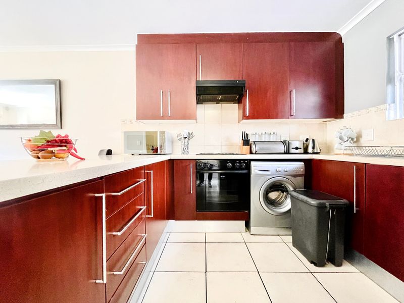 A functional kitchen featuring dark wood cabinetry, stone countertops, tiled flooring, and integrated appliances including an oven and extractor fan.