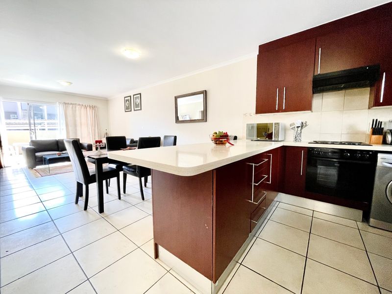 Open-plan living and kitchen area featuring dark wood cabinetry, stone countertops, built-in appliances, and tiled flooring with access to a balcony.