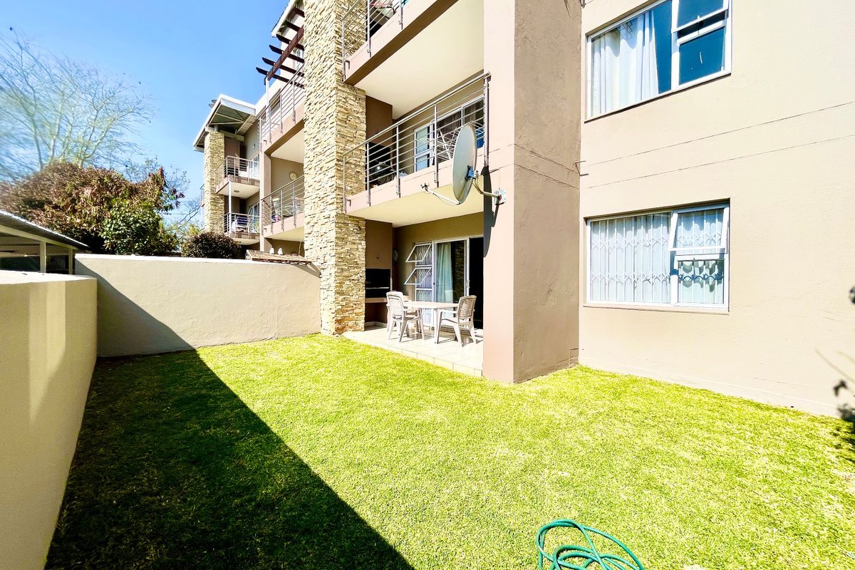 Rear view of the apartment building featuring a private garden, ground floor patio with built-in braai, and stone-clad architectural detailing.