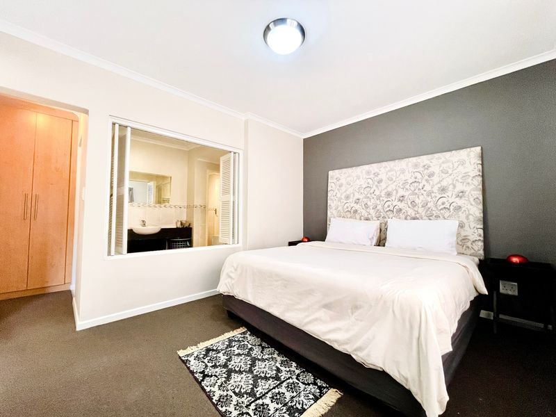 A well-maintained bedroom featuring carpeted flooring, built-in cupboards, and a large window providing a view into the adjoining en-suite bathroom.